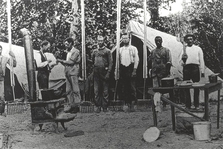 White men with rake like tools standing near tents and tables