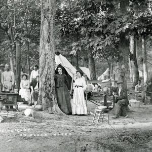 White men and women with camping tents and stove in wooded area