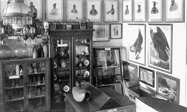Cabinets filled with items and framed drawings of Native Americans and birds on the walls