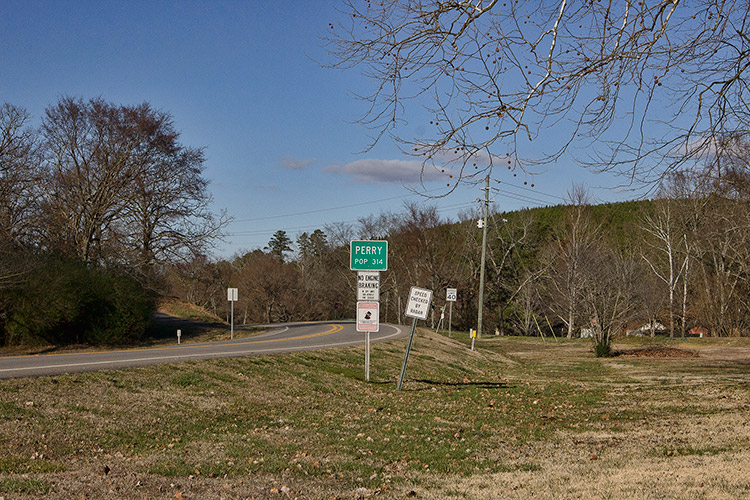 Highway curve section with road signs on both sides including green "Perry" sign