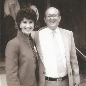 White woman smiling in suit standing with white man smiling in suit and glasses