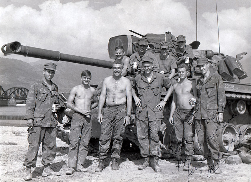 Group of young white men in military uniform and shirtless posing with tank