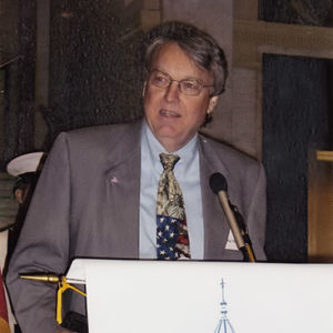 White man with glasses in suit speaking at lectern