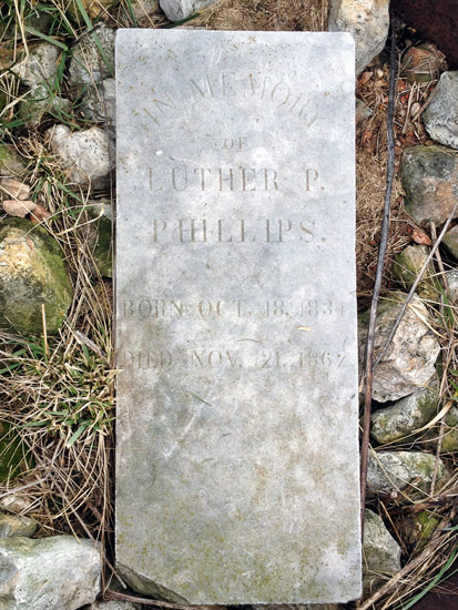 Stone grave marker on the ground with rocks and grass