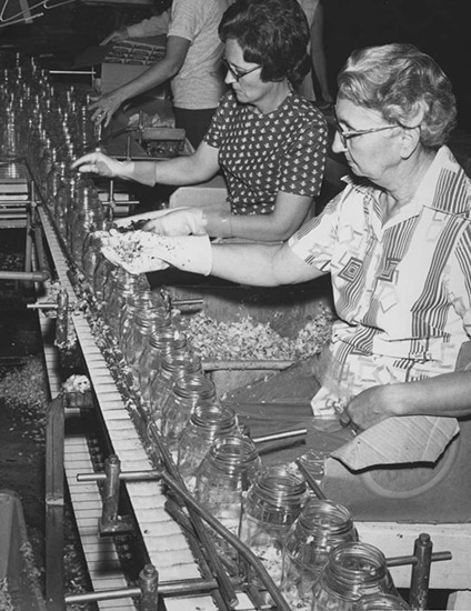 White women with glasses working at assembly line of jars