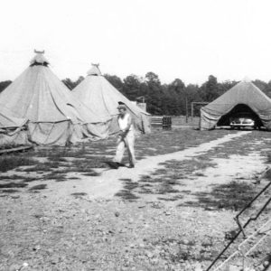 White man wearing German military helmet walking between rows of tents