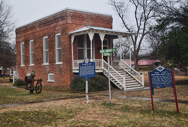 Brick building with covered porch stairs and historic marker sign