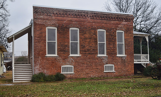 Side vide of brick building with row of windows and covered porch on both ends