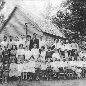 Group of white man women and children with single-story building behind them