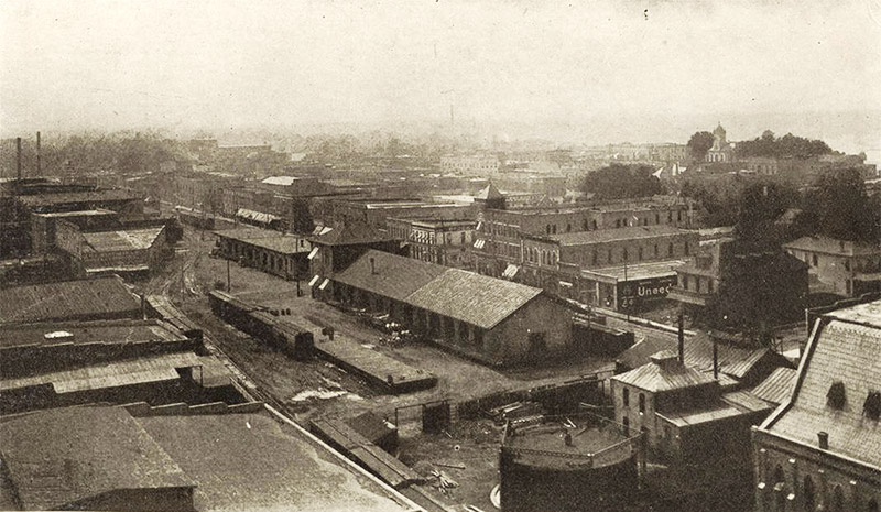 View overlooking multistory town buildings with train depot and rail yard in the foreground