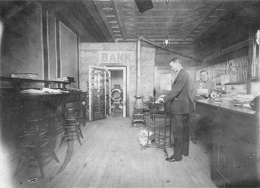 Two white men in suits working inside bank with open vault in the background