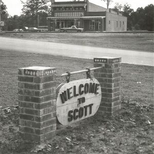 Multistory brick building with "Welcome to Scott" sign in the foreground