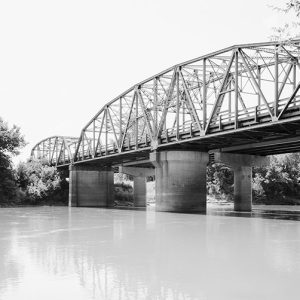 View from river bank of steel arch bridge with concrete supports in water