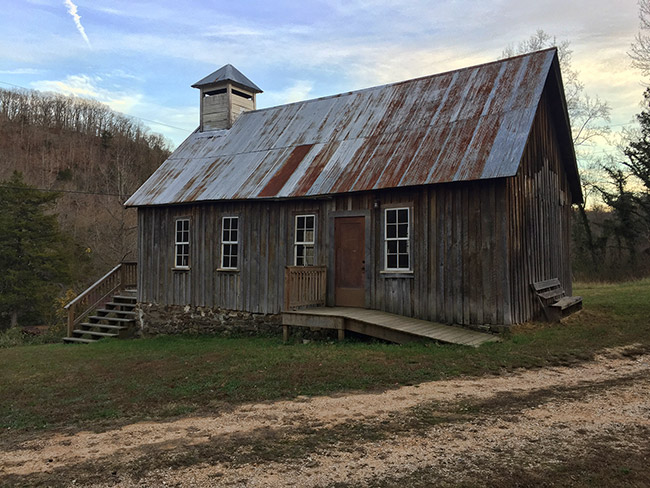 Wooden church building with sheet metal roof and cupola and wheelchair ramp on dirt road