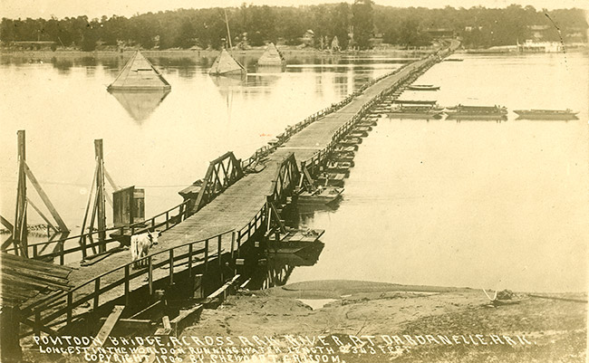 Pontoon bridge with wooden railings on river with boats