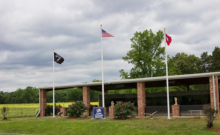 Memorial wall under pavilion with brick columns and three flag poles outside it