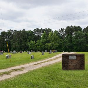 Dirt road through cemetery with brick signs under power lines
