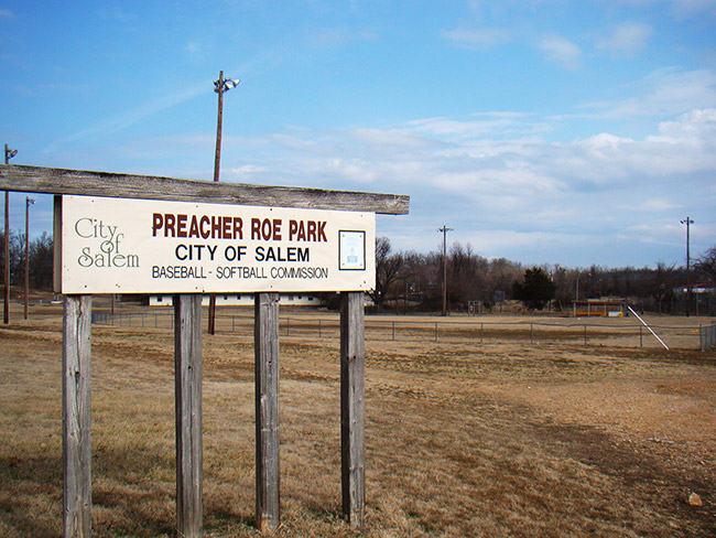 "Preacher Roe Park" sign with baseball field and lights in the background