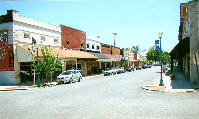 Brick storefronts with awnings on street with parked cars