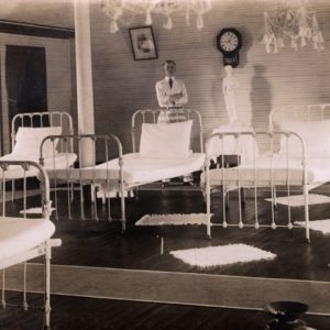 White man in suit standing in room full of hospital beds