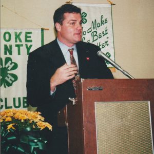 White man in suit speaking into microphone