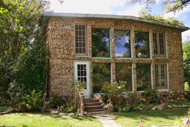 Two-story stone house with large windows and green foliage