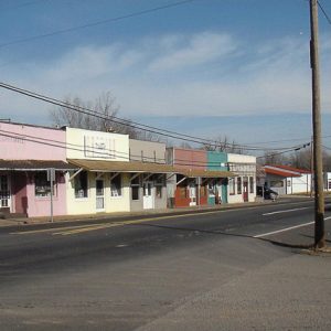 Line of single-story storefronts painted various colors on street