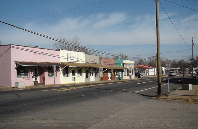 Line of single-story storefronts painted various colors on street