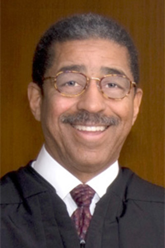 African-American man with glasses smiling in judge's robes