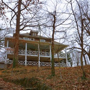 Front view of multiple story cabin on hill side with trees and steps covered in leaves