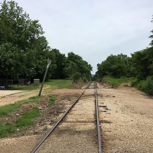 Railroad tracks on dirt and sign in lot with fence