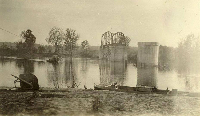Ferry on river next to steel arch bridge with concrete supports under construction