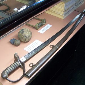 Cavalry sword and scabbard with cannon balls and books in display case