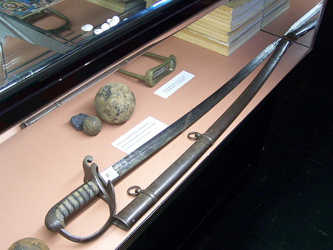 Cavalry sword and scabbard with cannon balls and books in display case