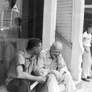 Two men casually sitting on a stoop conversing, one of whom is laughing.