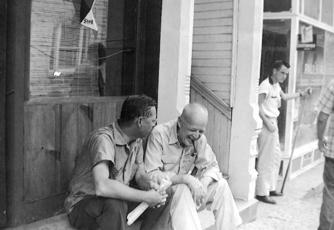 Two men casually sitting on a stoop conversing, one of whom is laughing.