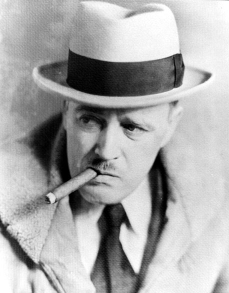 White man with mustache wearing a fedora hat and suit smoking a cigar