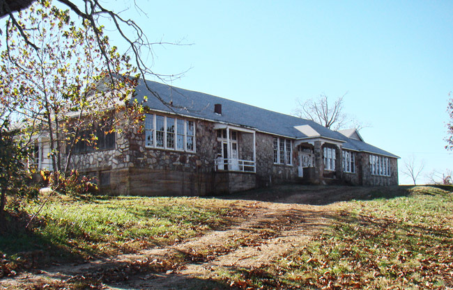 Single-story building with stone walls and covered porches on dirt driveway