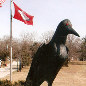 Bird statue surrounded by bushes with Arkansas and American flags