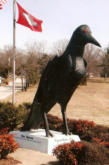 Bird statue surrounded by bushes with Arkansas and American flags
