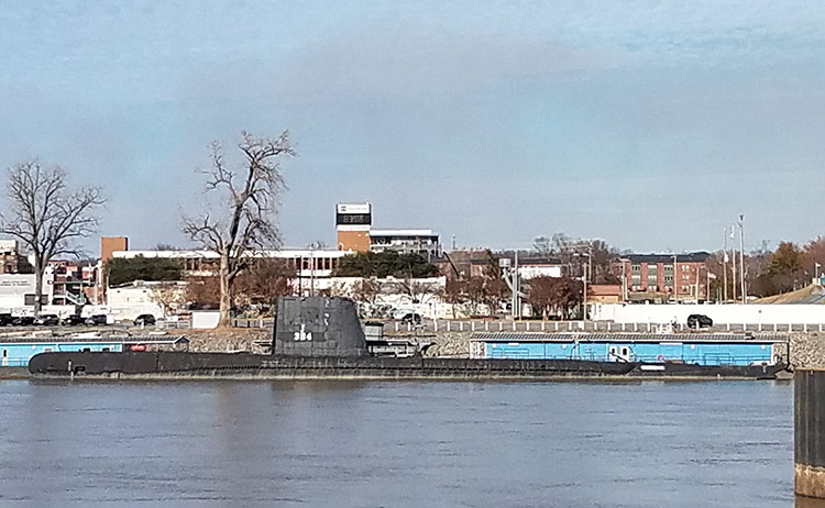 Submarine in river with dock and city buildings in the background