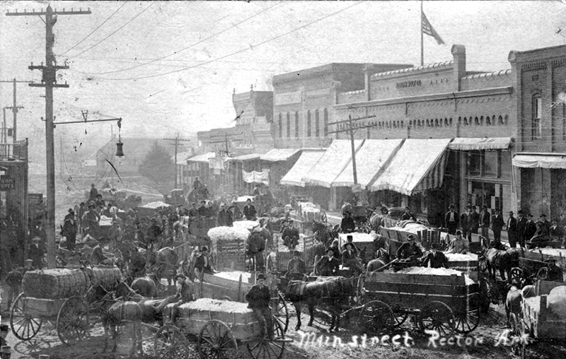 Horse drawn wagons loaded with cotton and white drivers in crowded town street
