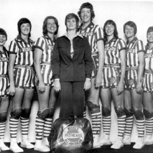 Group of white women in striped uniforms and coach in jacket with bag in foreground "Moore's Redheads All American"