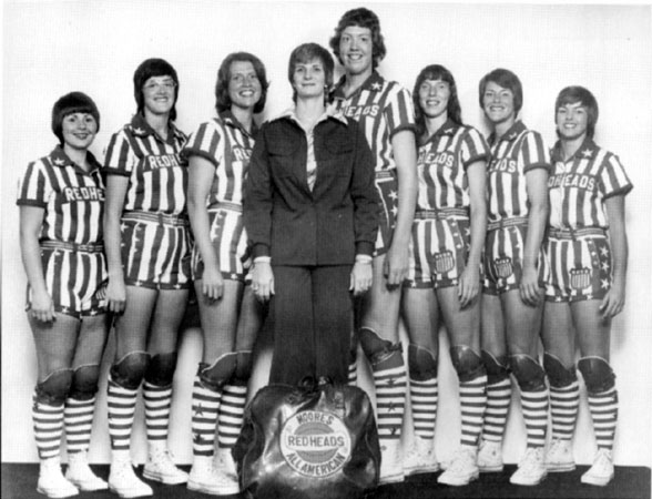Group of white women in striped uniforms and coach in jacket with bag in foreground "Moore's Redheads All American"