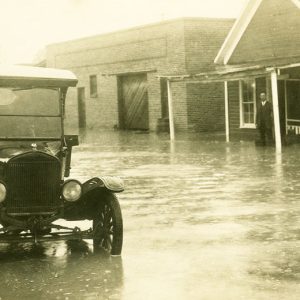 Black car parked on flooded street with two people standing in the waters in the distance