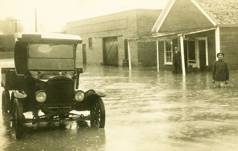 Black car parked on flooded street with two people standing in the waters in the distance
