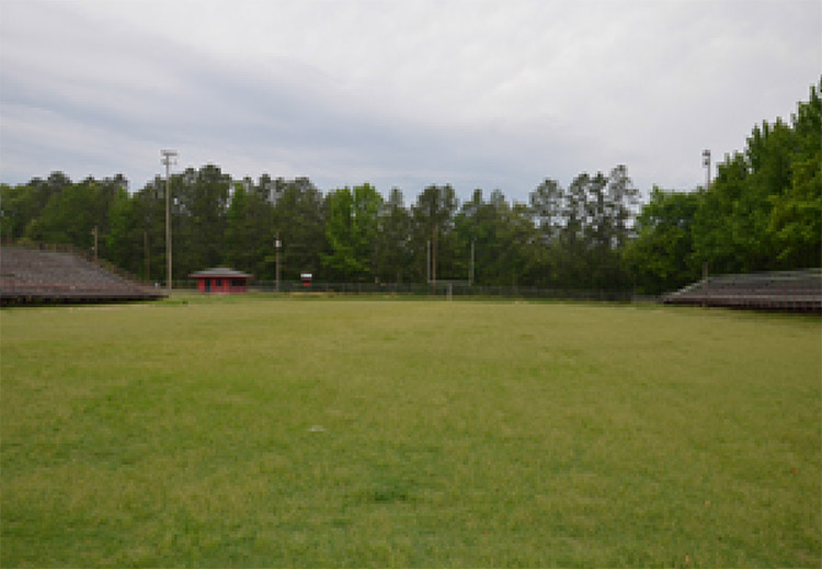 Vacant football field with bleachers on either side and goal in the background along a fence