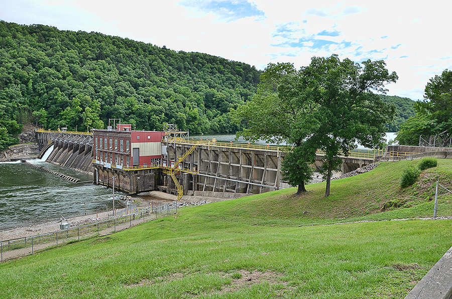 Concrete dam and turbine room on river with forested hillside in background