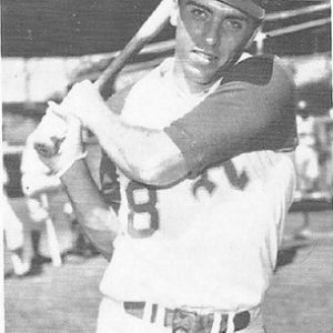 White man in baseball uniform swinging a bat on field