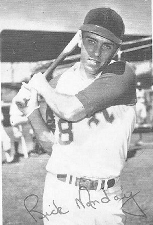 White man in baseball uniform swinging a bat on field